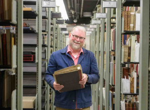 Eric Johnson-DeBaufre, Rare Books and Special Collections Librarian for the Watkinson Library at Trinity College, poses with a collection of scraps from the archives containing a page from an Aelius Donatus.