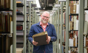 Eric Johnson-DeBaufre, Rare Books and Special Collections Librarian for the Watkinson Library at Trinity College, poses with a collection of scraps from the archives containing a page from an Aelius Donatus.